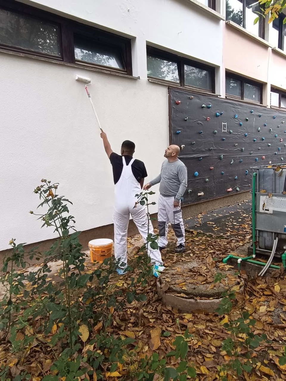 Učenik boji zid valjkom uz podršku nastavnika